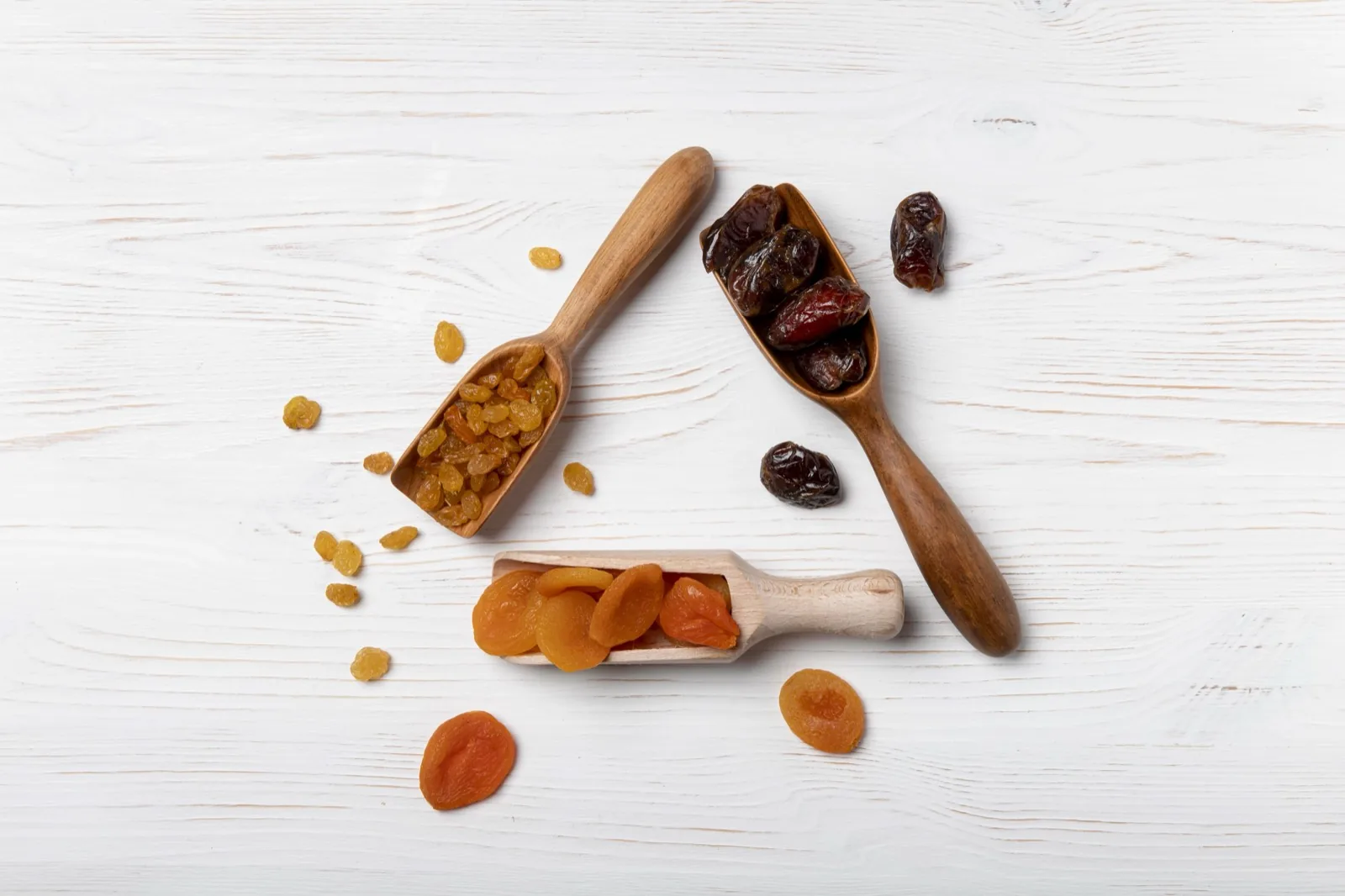 Wooden scoops of golden raisins, dates and dried apricots