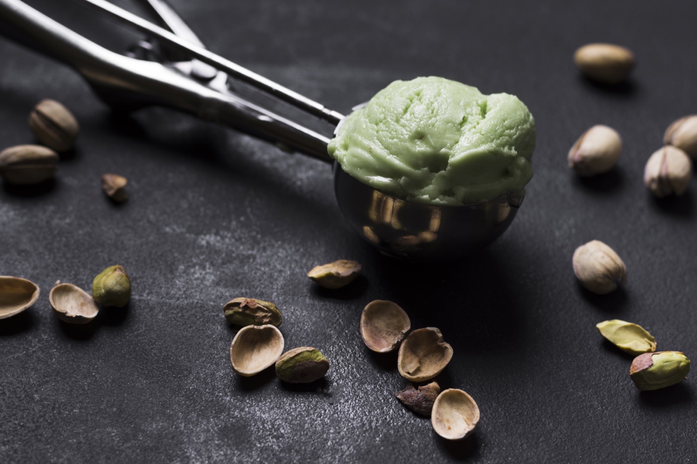 Scoop of pistachio ice cream with a metal scoop, pistachios alongside