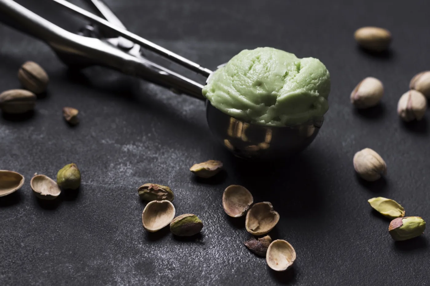 Scoop of pistachio ice cream with a metal scoop, pistachios alongside